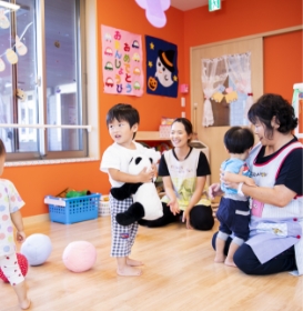 オレンジ色の壁の明るい室内で、複数の入居者がスタッフと一緒にレクリエーション活動を行っている様子